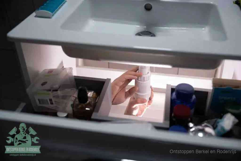 Een pompfles met zeep boven een wastafel, de heet water en afwasmiddel-methode om een vetprop in de afvoer los te maken in Berkel en Rodenrijs