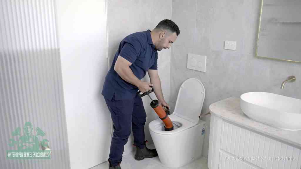 Een monteur buigt over een wandcloset en duwt met de hand een persluchtontstopper in de toiletpot om de verstopping handmatig los te maken in Berkel en Rodenrijs