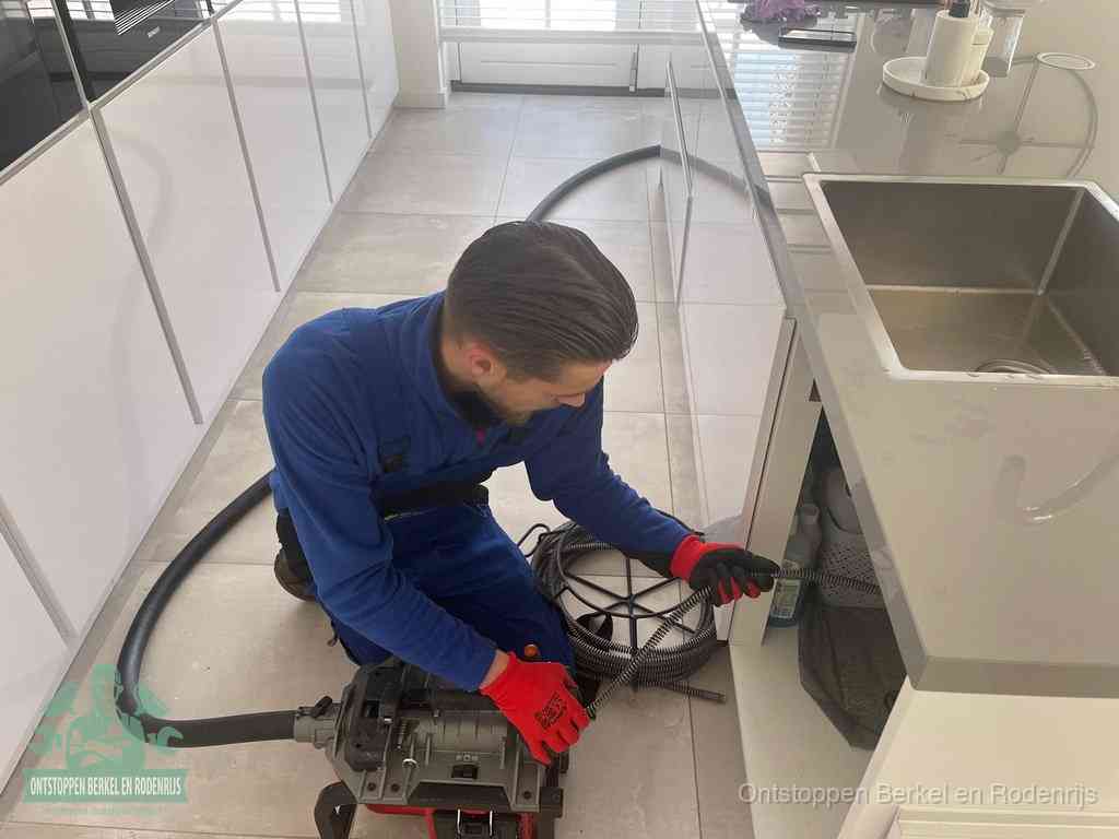 Een monteur ontstopt de keukenafvoer onder de spoelbak met een elektrische veermachine in Berkel en Rodenrijs