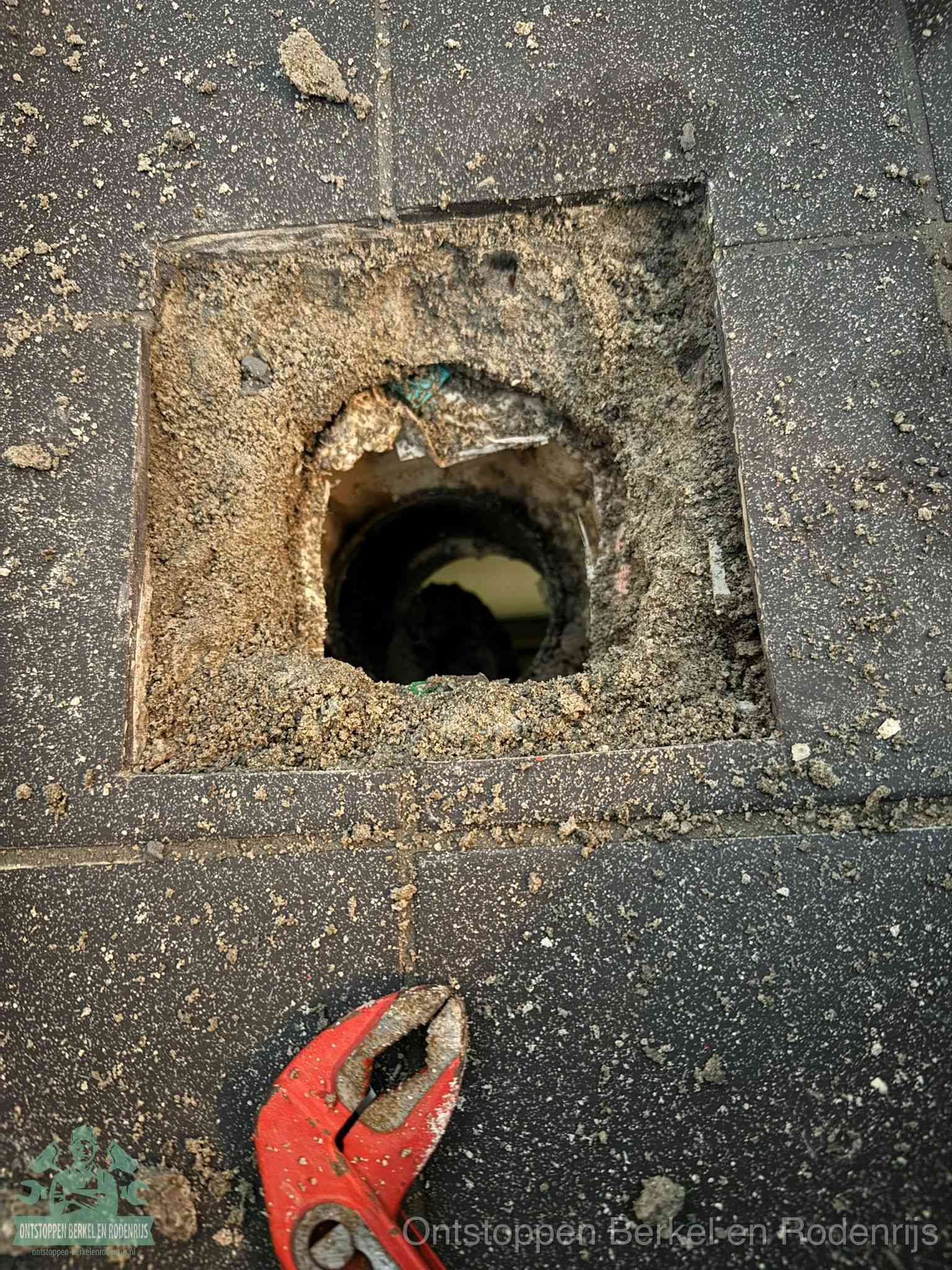 Een geopend rioolputje in een betontegelvloer met losgemaakt rooster en een zichtbare ronde afvoerbuis, het achterhalen waar de afvoerverstopping zit in Berkel en Rodenrijs