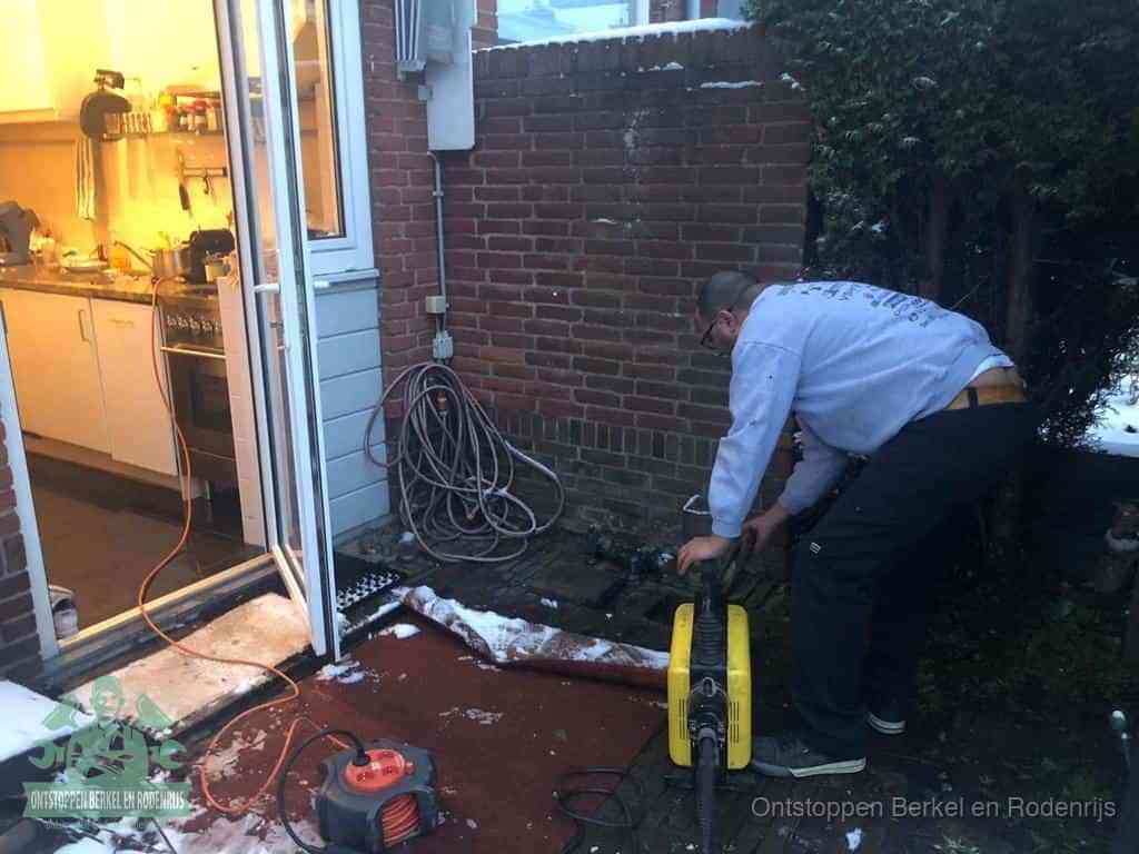 Een monteur werkt buiten bij een open riool-/grondput met een elektrische ontstoppingsmachine om een verborgen afvoerprobleem op te sporen in Berkel en Rodenrijs