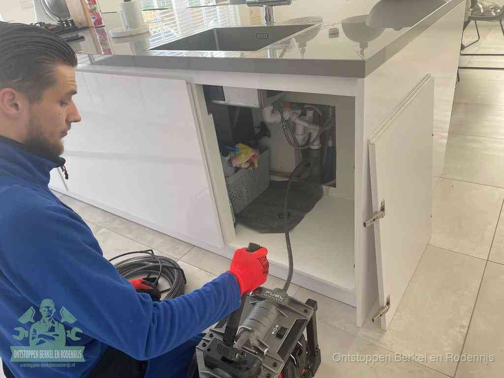 Monteur ontstopt met een veermachine een verstopte afvoer onder de gootsteen in Berkel en Rodenrijs
