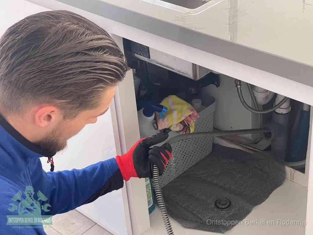 Een monteur voert een flexibele ontstoppingsveer in de afvoer om een verstopping voorbij de bocht van het toilet te bereiken in Berkel en Rodenrijs