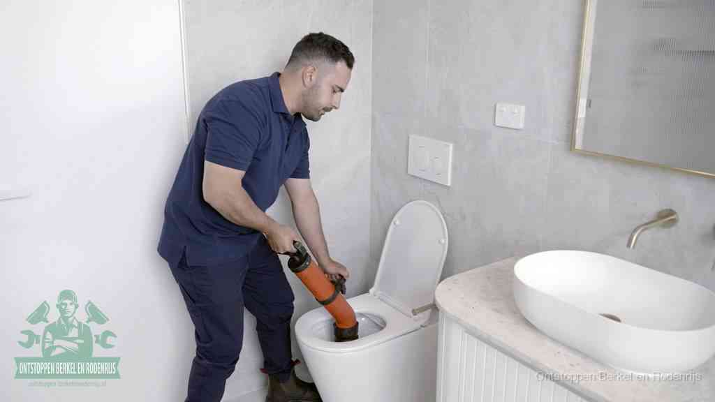 Een man gebruikt een handmatige luchtdruk-ontstopper in een modern betegeld toilet om zelf de wc te ontstoppen in Berkel en Rodenrijs